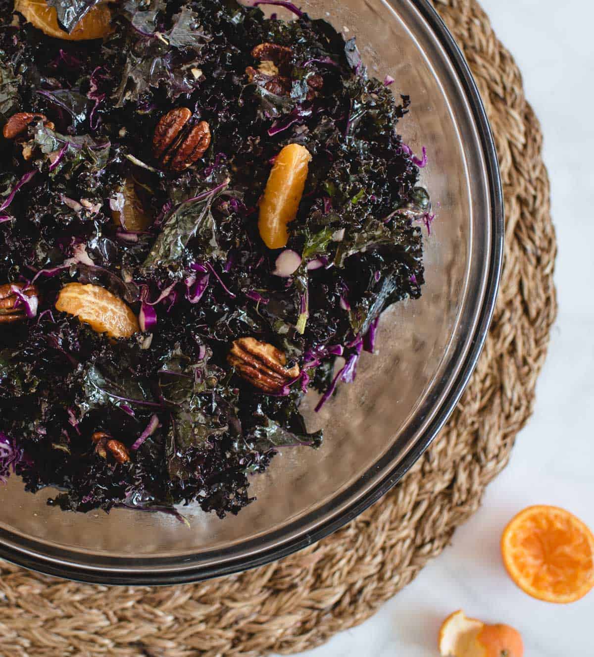 close up overhead shot of kale salad in a large serving bowl tossed with pieces of mandarin oranges and pecans