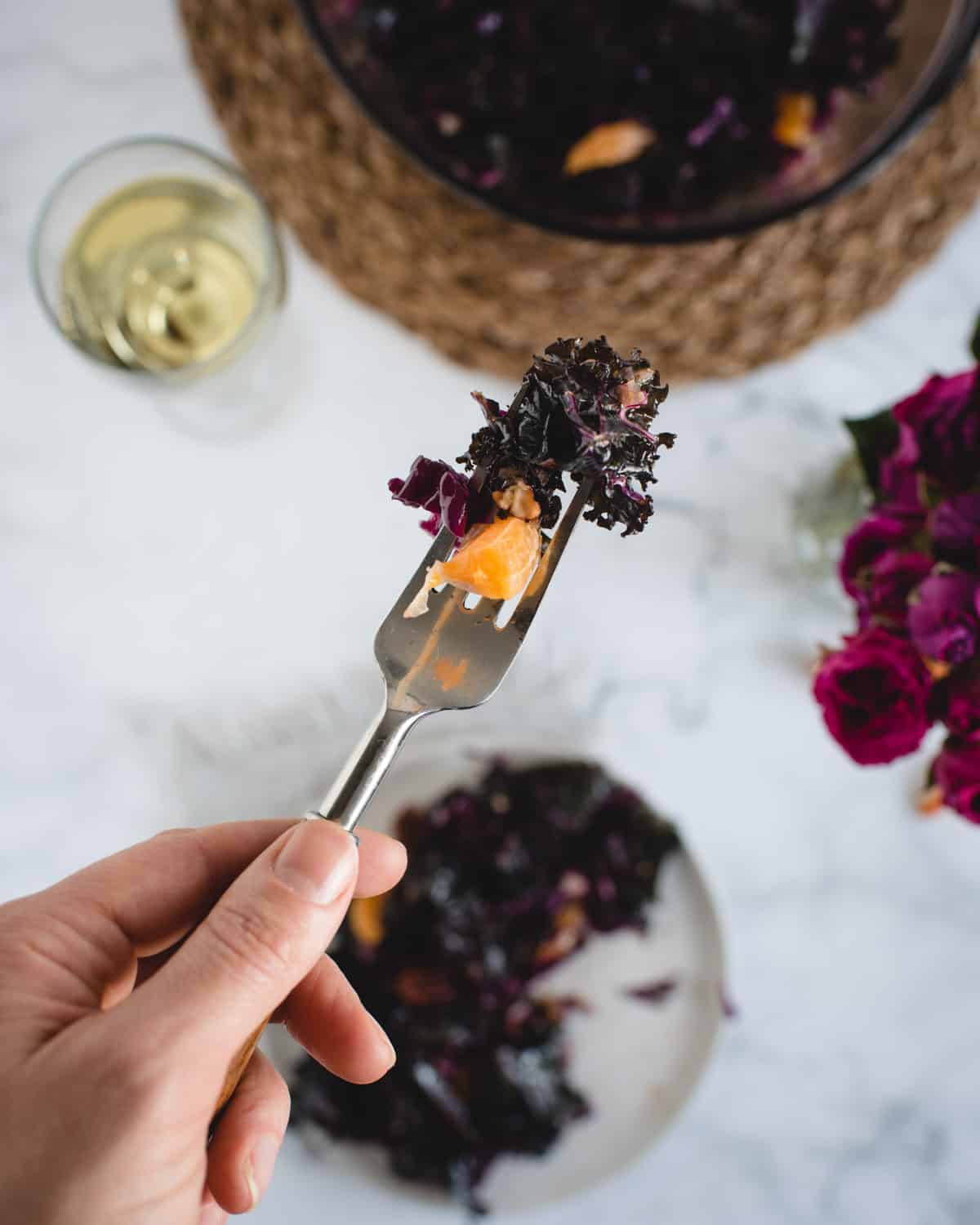 bite of kale salad with mandarin orange and pecans lifted up on a fork by a hand against a white background 