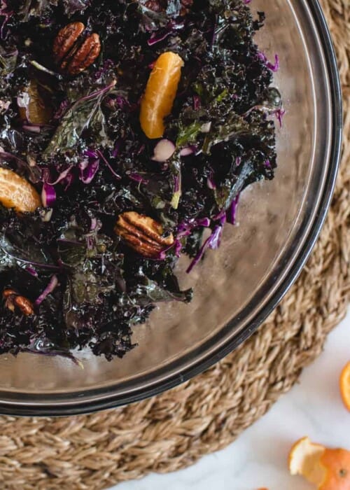 close up overhead square shot of large glass bowl of kale salad with mandarins