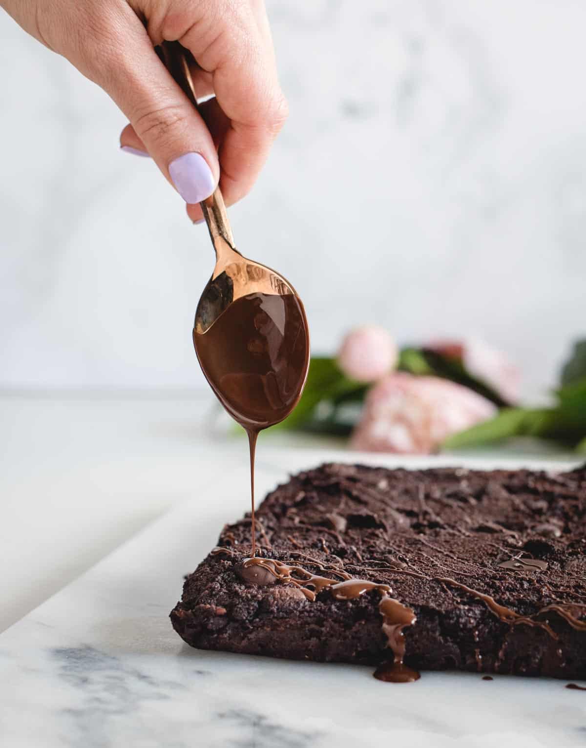 spoon drizzling melted chocolate onto brownies