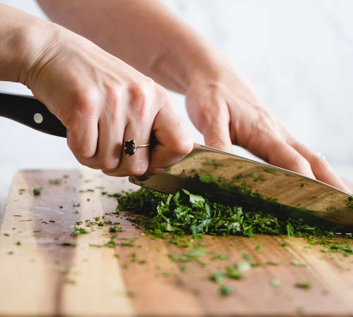 Hands chopping fresh herbs with a knife on a cutting board