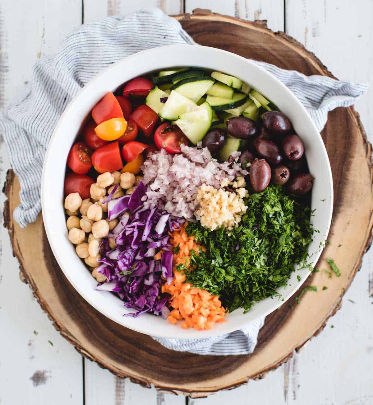 Pre-tossed salad ingredients grouped separately within a bowl on a wood white background