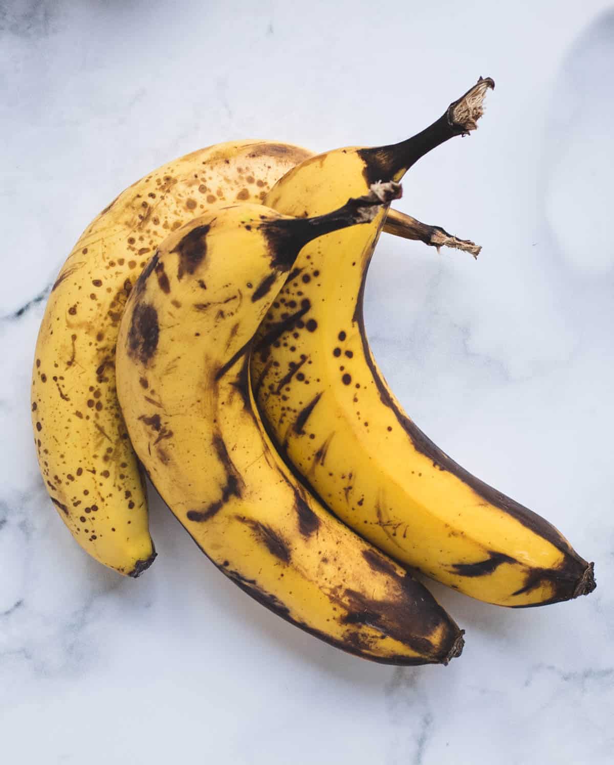 over ripe bananas with brown spots on a marble white backdrop