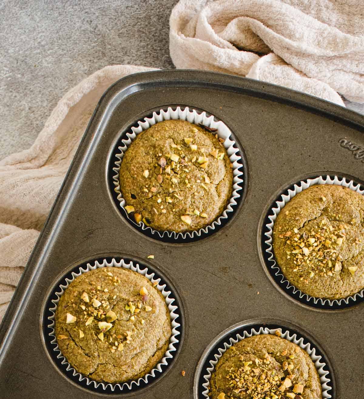 overhead of muffins in a muffin tin with crushed pistachios sprinkled on top