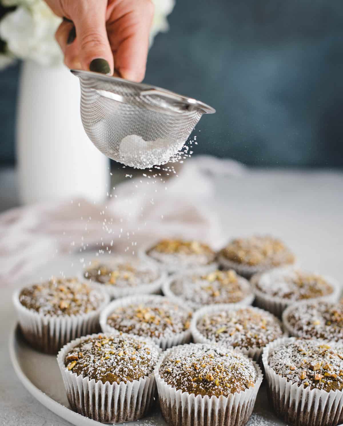 Hand using small sieve strainer to sprinkle powdered sugar on muffins