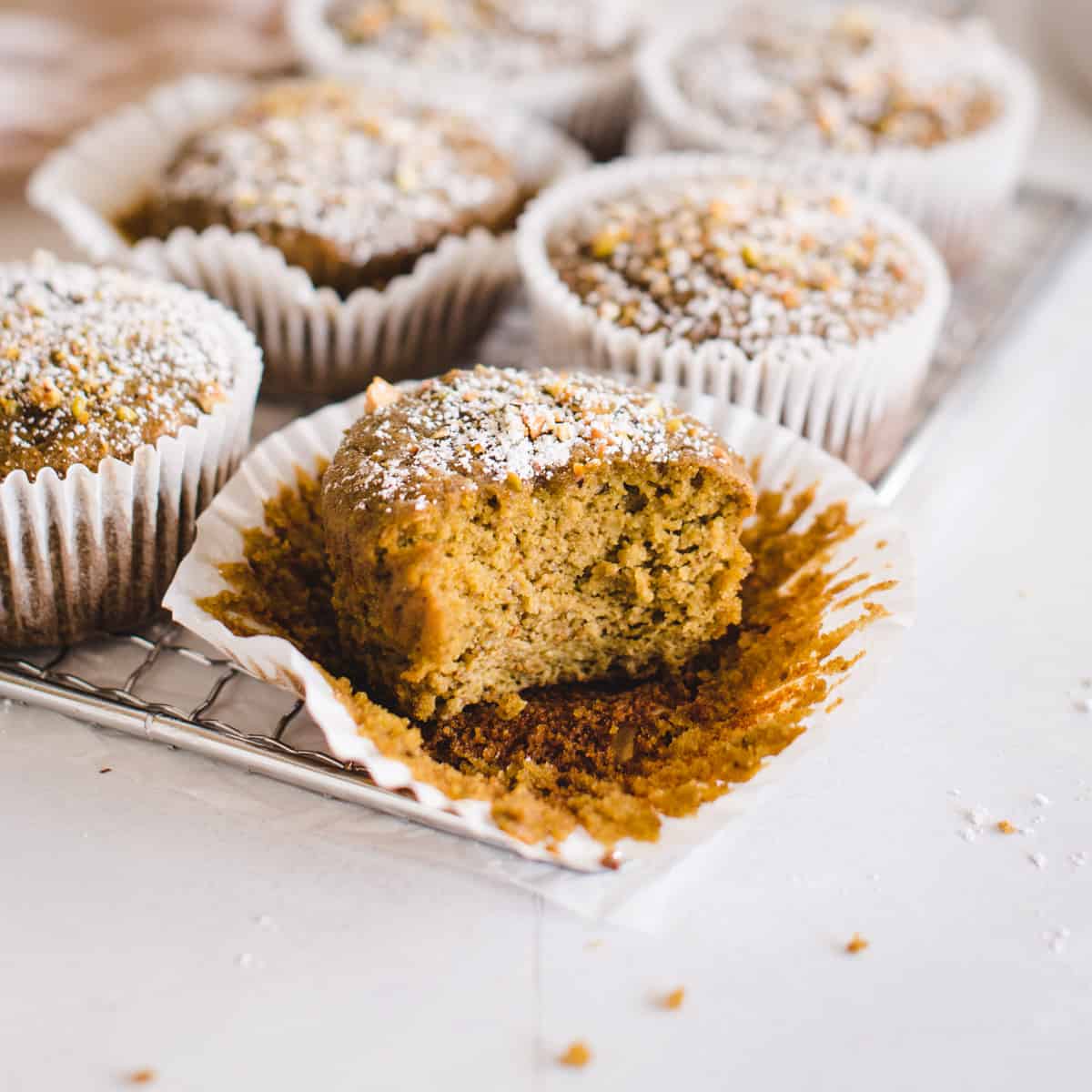 close up of a pistachio muffin sitting on a muffin wrapper with a bite missing