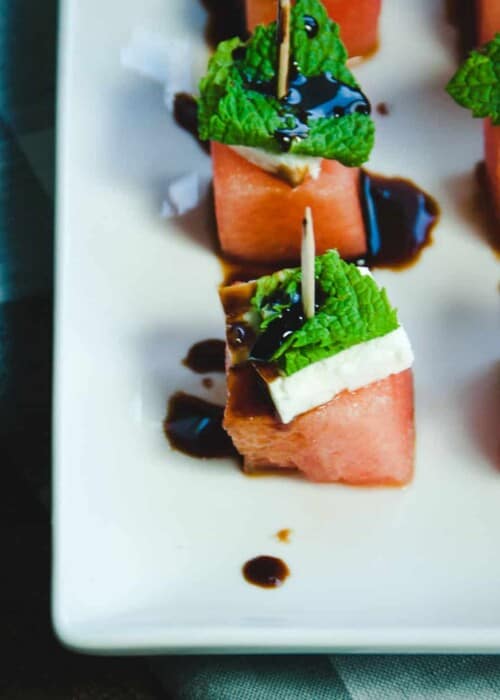 watermelon skewered on a toothpick with feta, mint and balsamic glaze