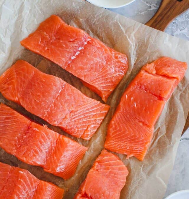close up of six strips of raw salmon on a cutting board