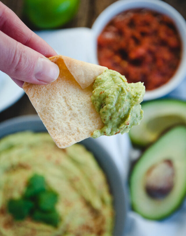 hand holding pita chip with avocado dip on it