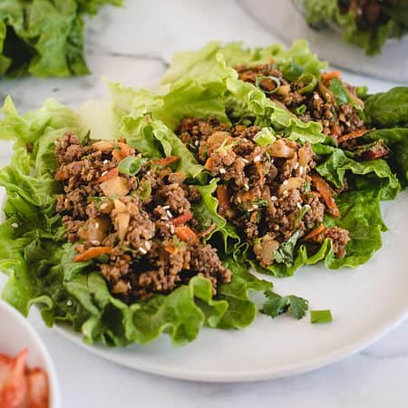 Lettuce wraps filled with minced meat, diced vegetables, and herbs on a white plate.