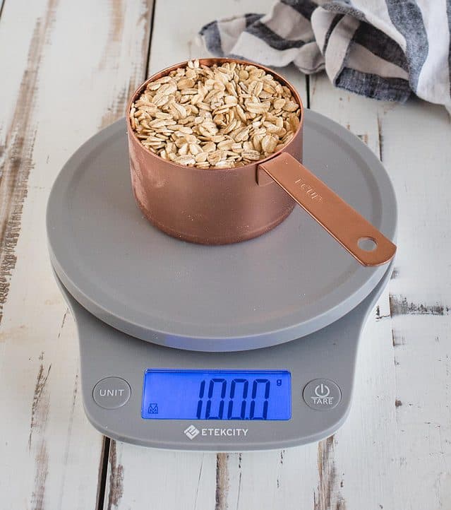measuring cup of oats a scale reading 100 grams