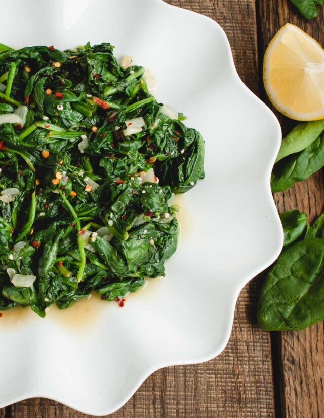 close up image of spinach on a white plate with lemon next to it
