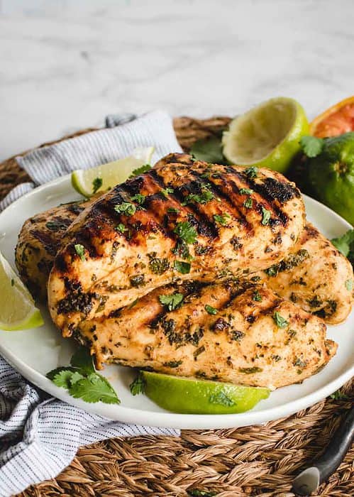 Mexican chicken on a plate with cilantro sprinkled on top and citrus in background