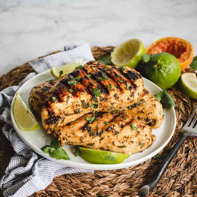Mexican chicken on a plate with cilantro sprinkled on top and citrus in background