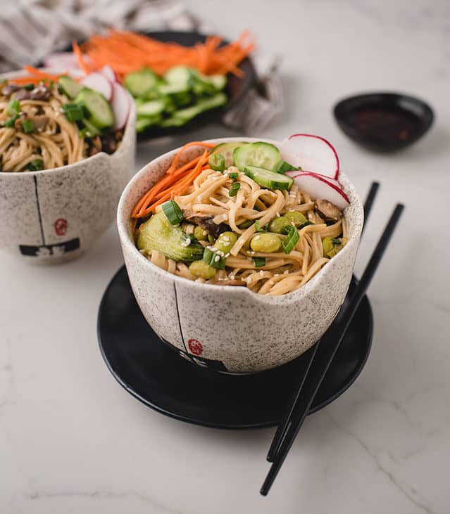 side angle of bowls of miso noodles topped with cucumber, carrot and raddish