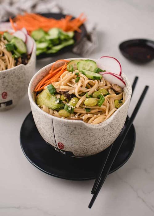 side angle of bowls of miso noodles topped with cucumber, carrot and raddish