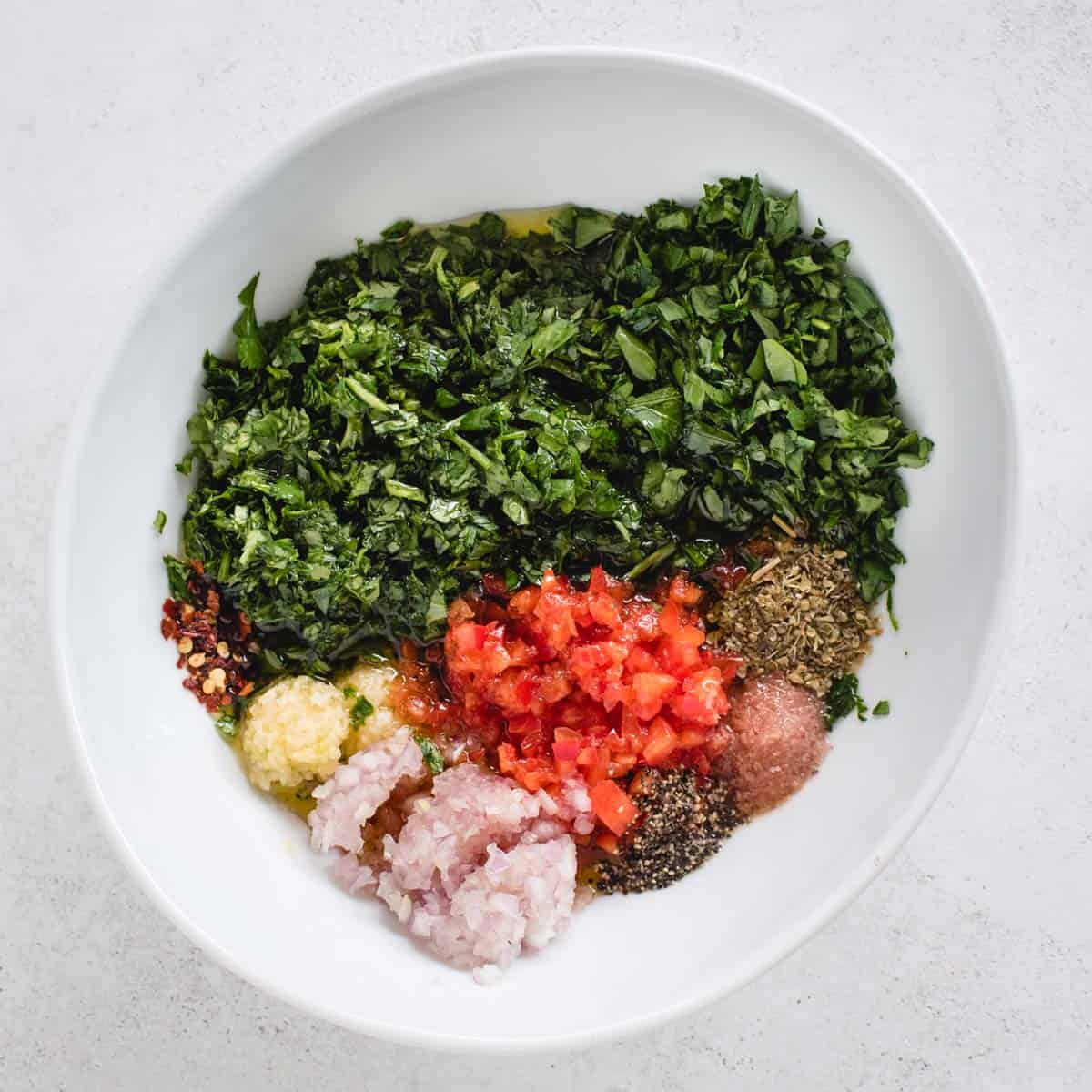 Fresh chopped herbs, red pepper, and other ingredients in a white bowl