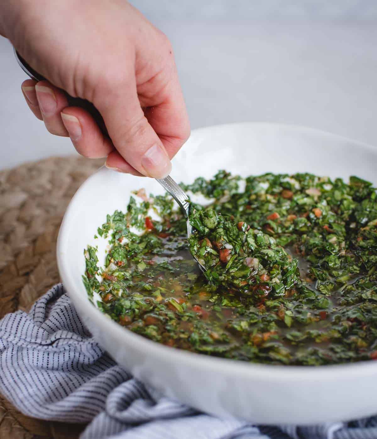 Hand scooping cilantro chimichurri from a white bowl
