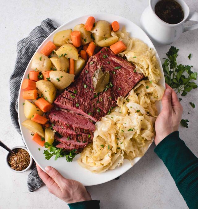 Hands setting down a platter of corned beef, cabbage, potatoes and carrots