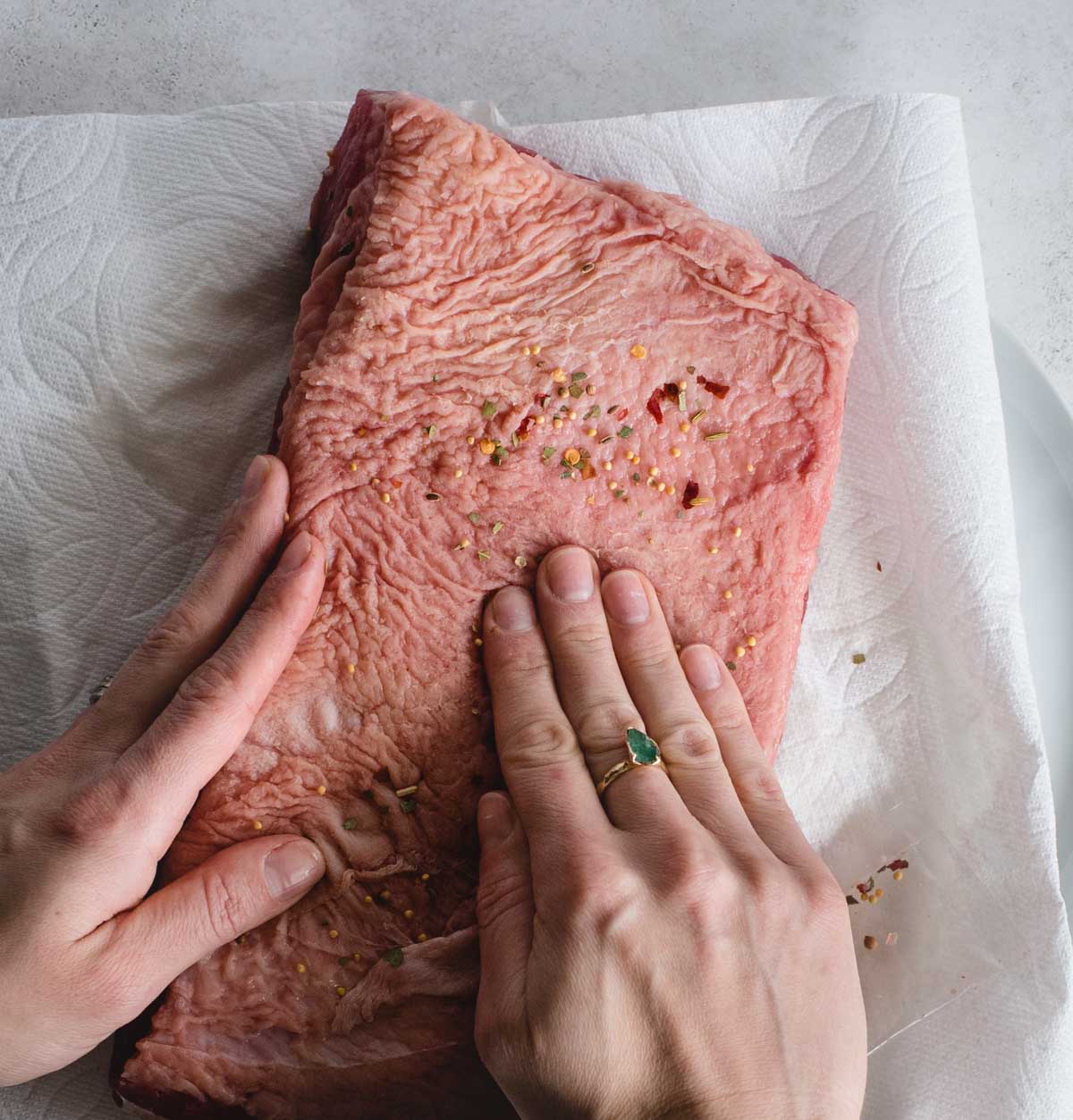 hands rubbing spices onto fatty side of corned beef