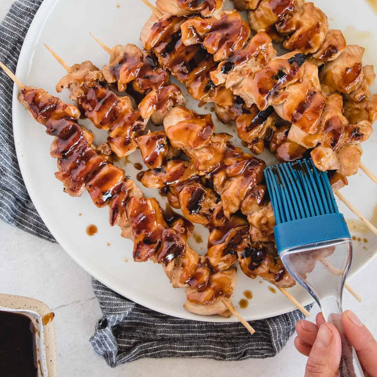 Grill brush spreading sauce onto chicken skewers