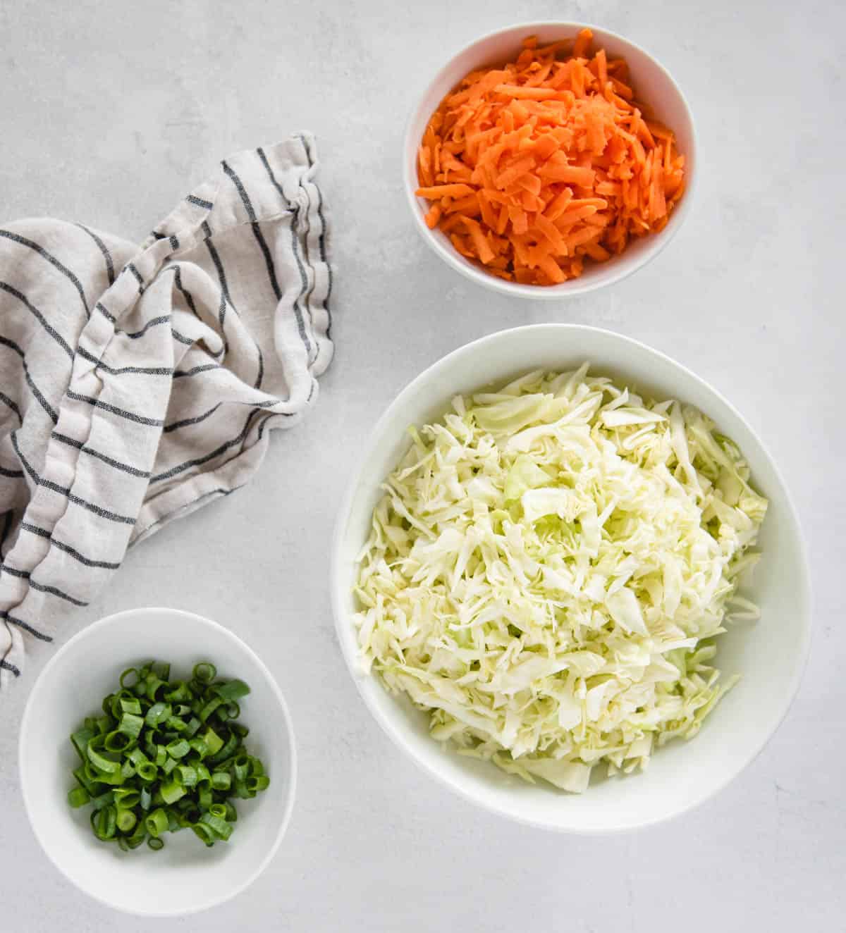 White bowls of cabbage, carrots, and green onion