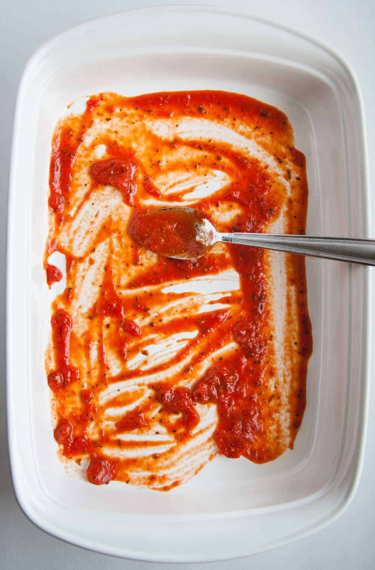 white baking dish with red sauce spread over the bottom