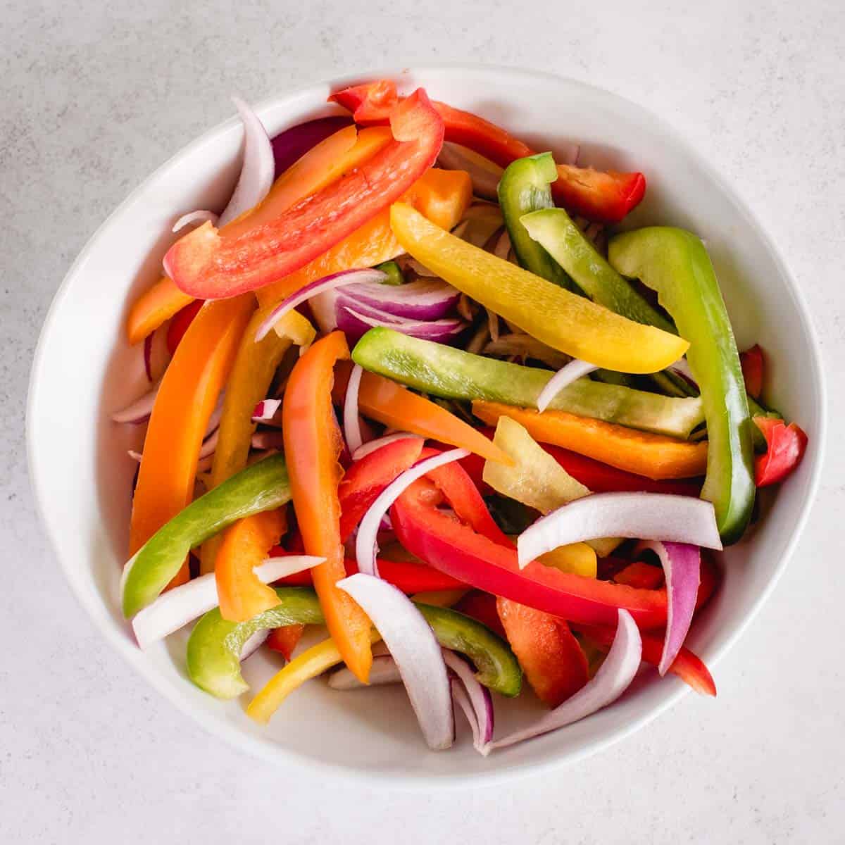 cut up raw sliced different colored peppers and red onion in a bowl