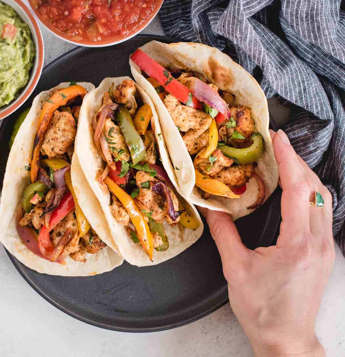 plate with 3 chicken fajitas on it with a hand grabbing one of them