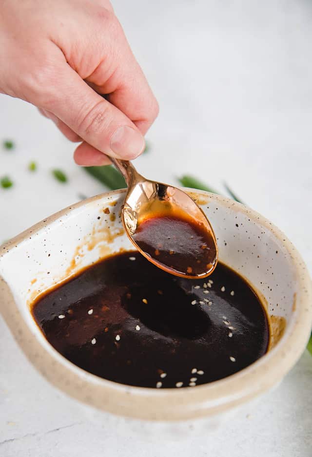 vertical side view of teriyaki sauce being lifted from a bowl by a spoon