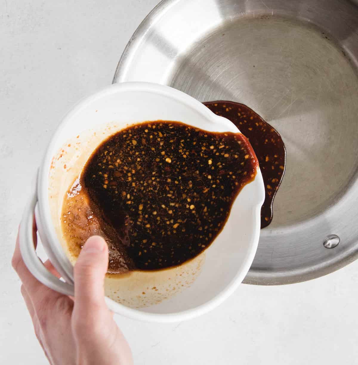 hand pouring teriyaki sauce into a pan from a dish