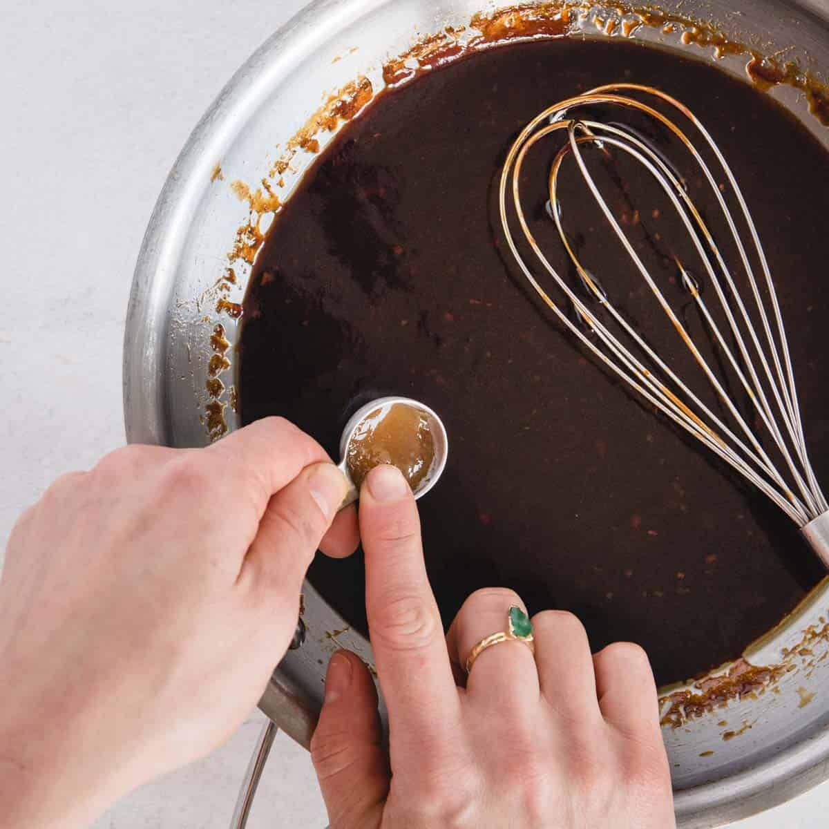 honey being added to a dark sauce in a pan
