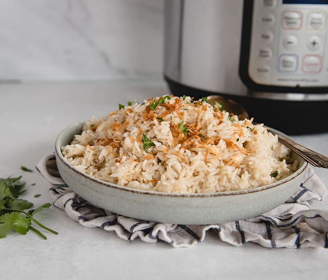 side view of coconut rice in a bowl with instant pot in background