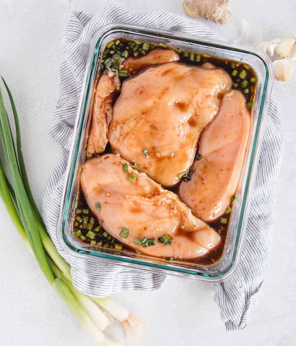 teriyaki chicken marinade with chicken breasts in it marinating with green onion on top