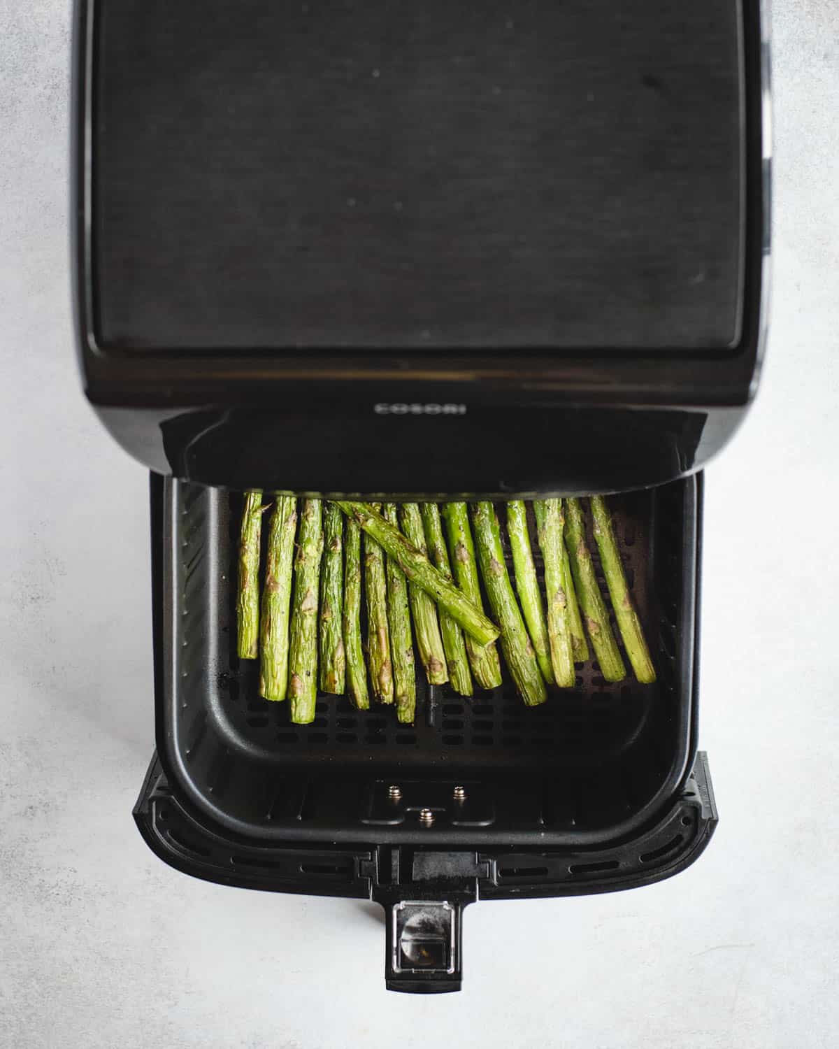 cooked asparagus in an air fryer basket that is half way pulled out of the air fryer