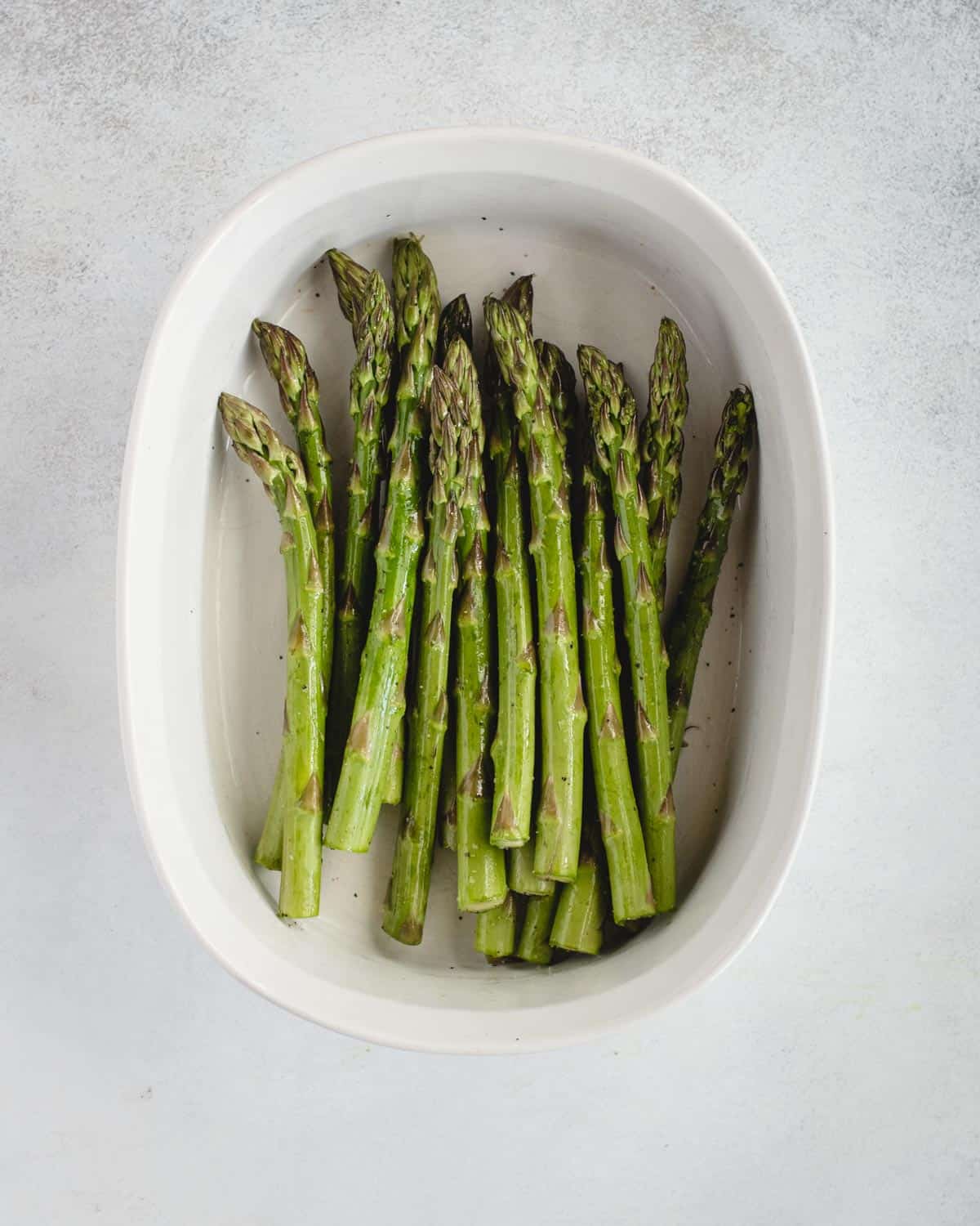asparagus in a baking dish tossed with pepper and oil