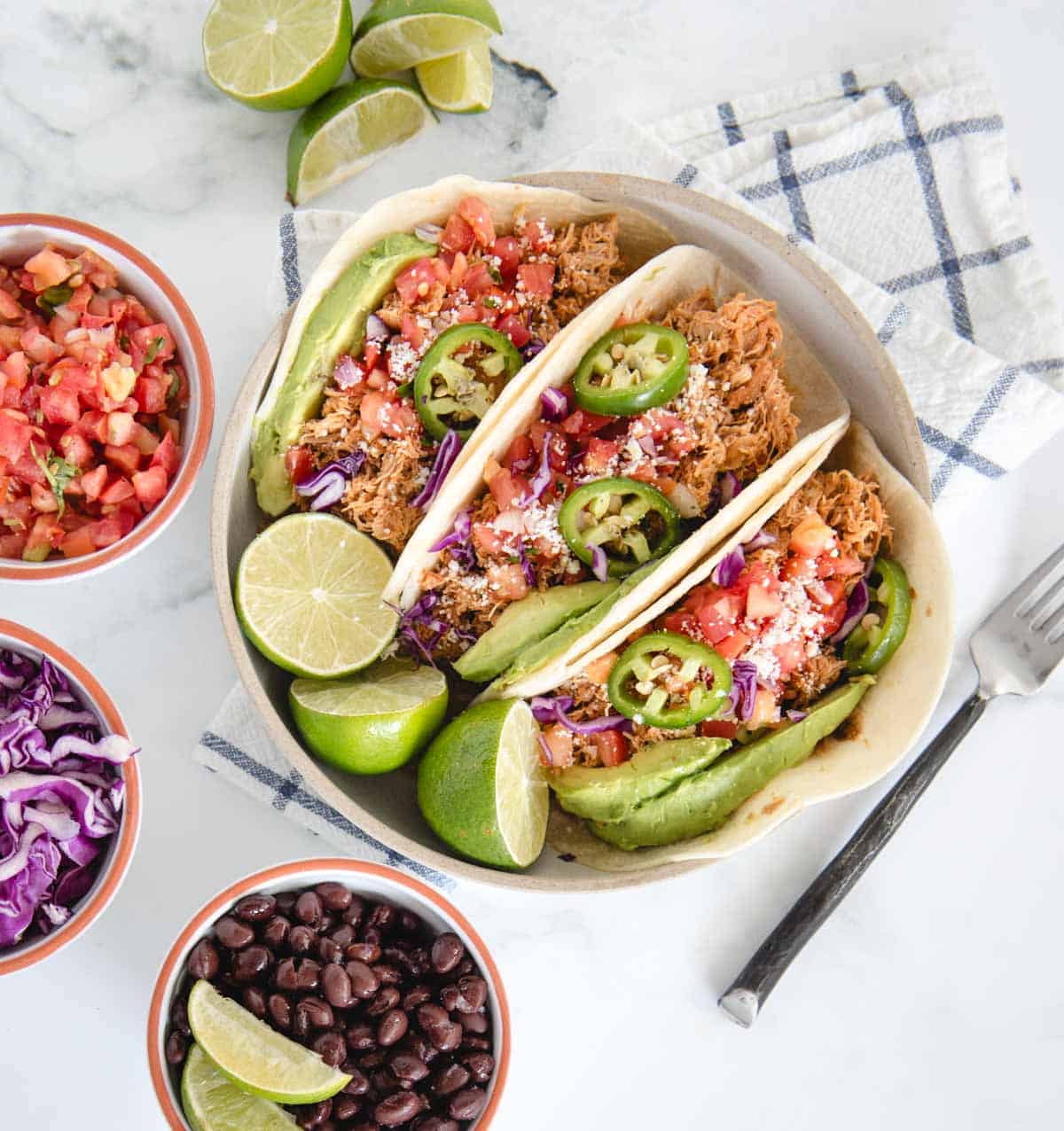 plate with shredded chicken tacos on it from overhead on white background with salsa, beans and cabbage on the side