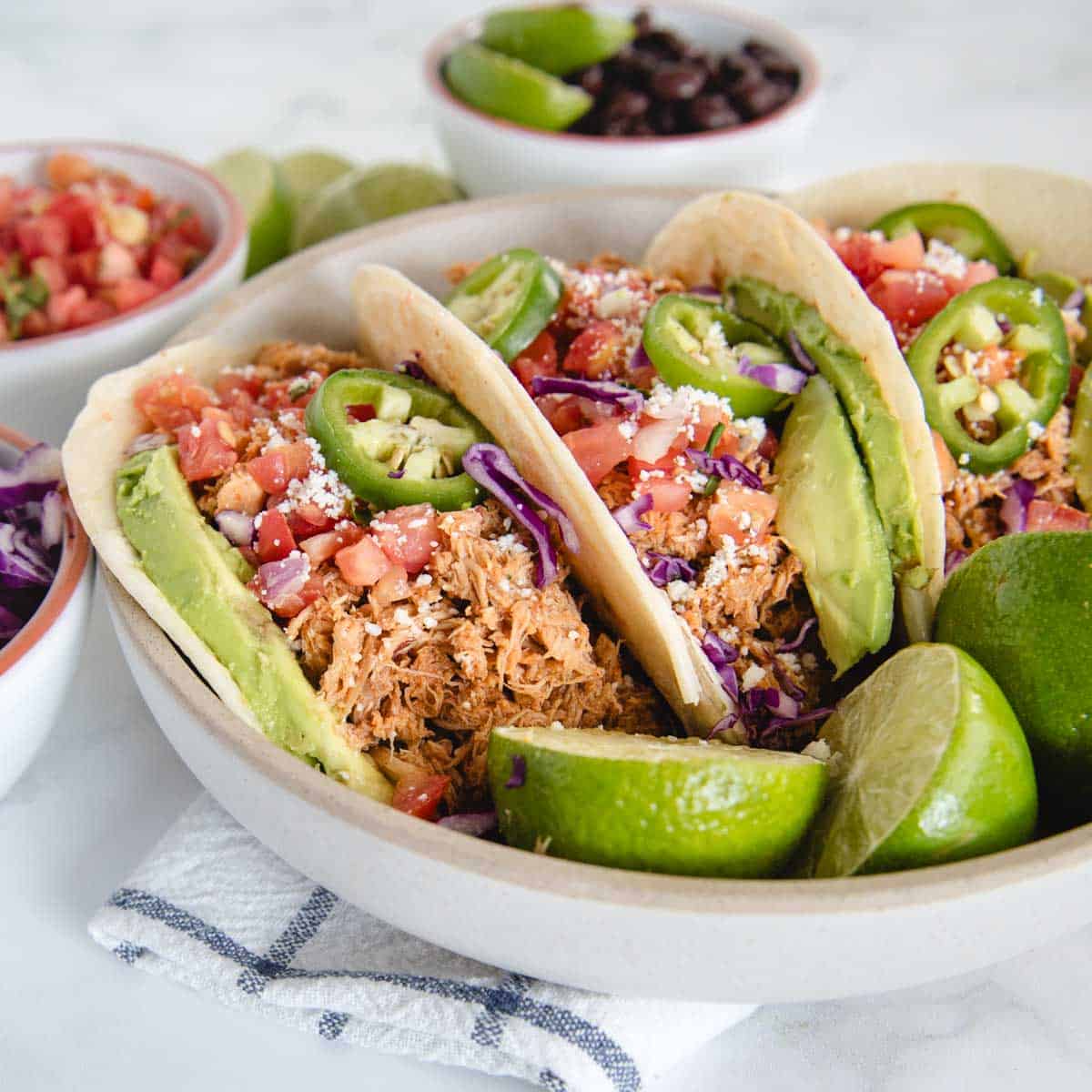 close up side view of 3 shredded crockpot chicken tacos next to limes