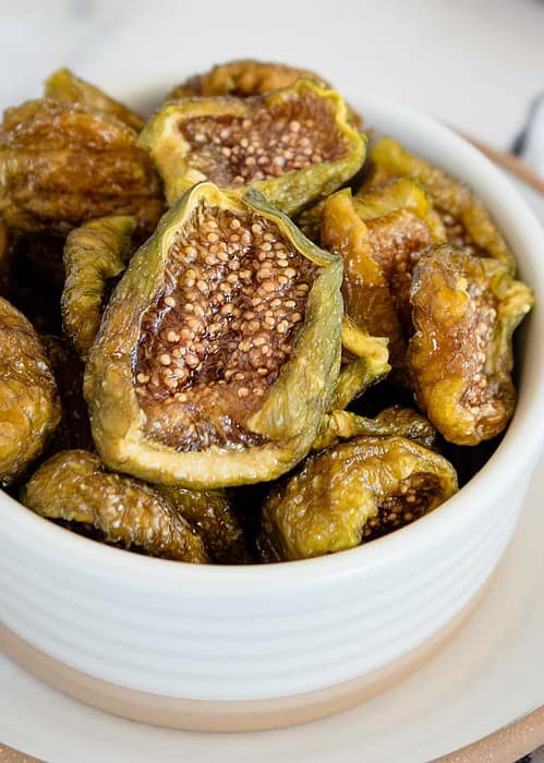 very close up image of a white bowl of dehydrated figs from the side view