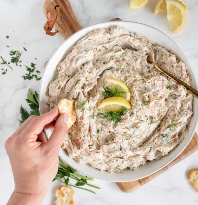 bowl of salmon dip from overhead angle with hand dipping cracker into it