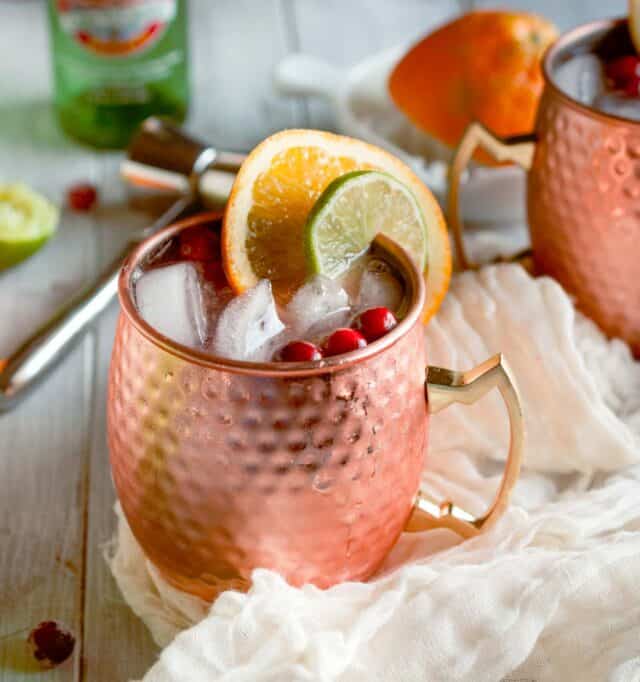 moscow mule in a copper mug from the side with lime and orange slices and cranberries