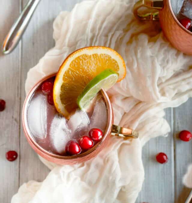 cranberry moscow mule in a copper mug from overhead with lime, orange and cranberry garnish