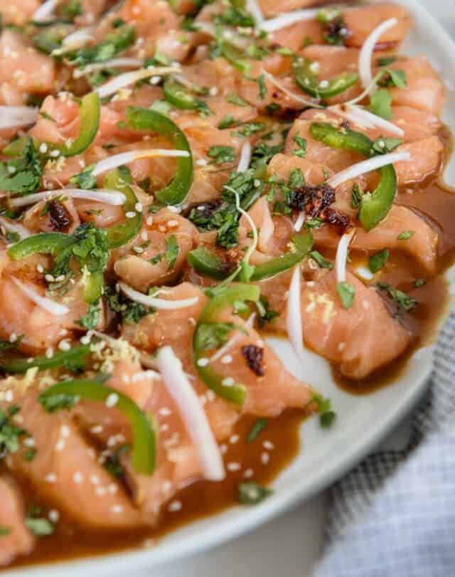 side view of plate with thinly sliced salmon crudo with lemon zest, shallot, cilantro and other garnishes with a soy sauce dressing
