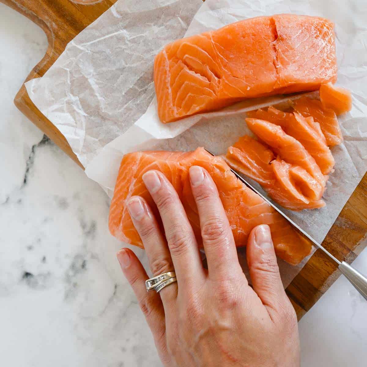 hand thinly slicing raw salmon against the grain on a cutting board