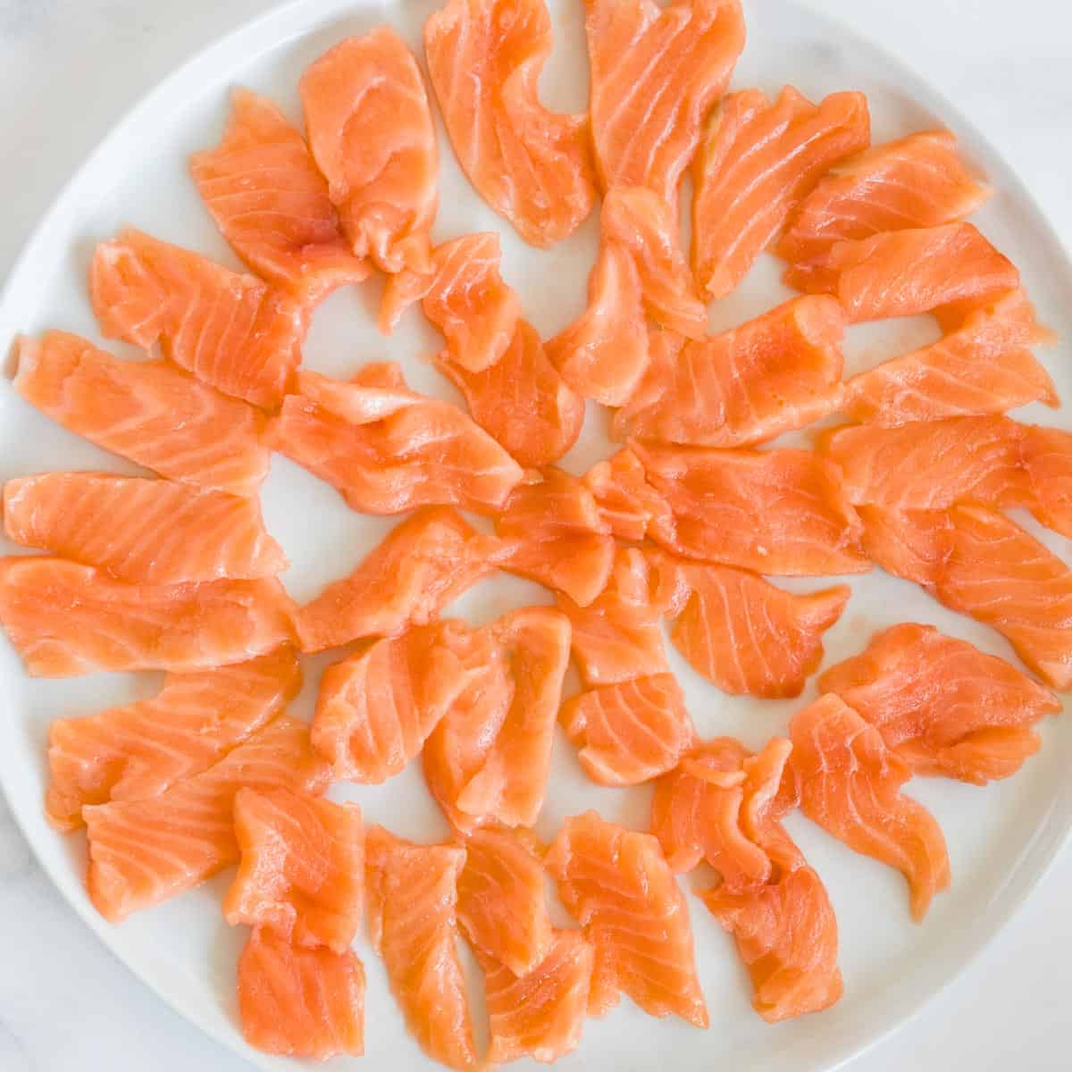 thinly sliced sushi grade salmon laid out in a circular pattern on a white plate