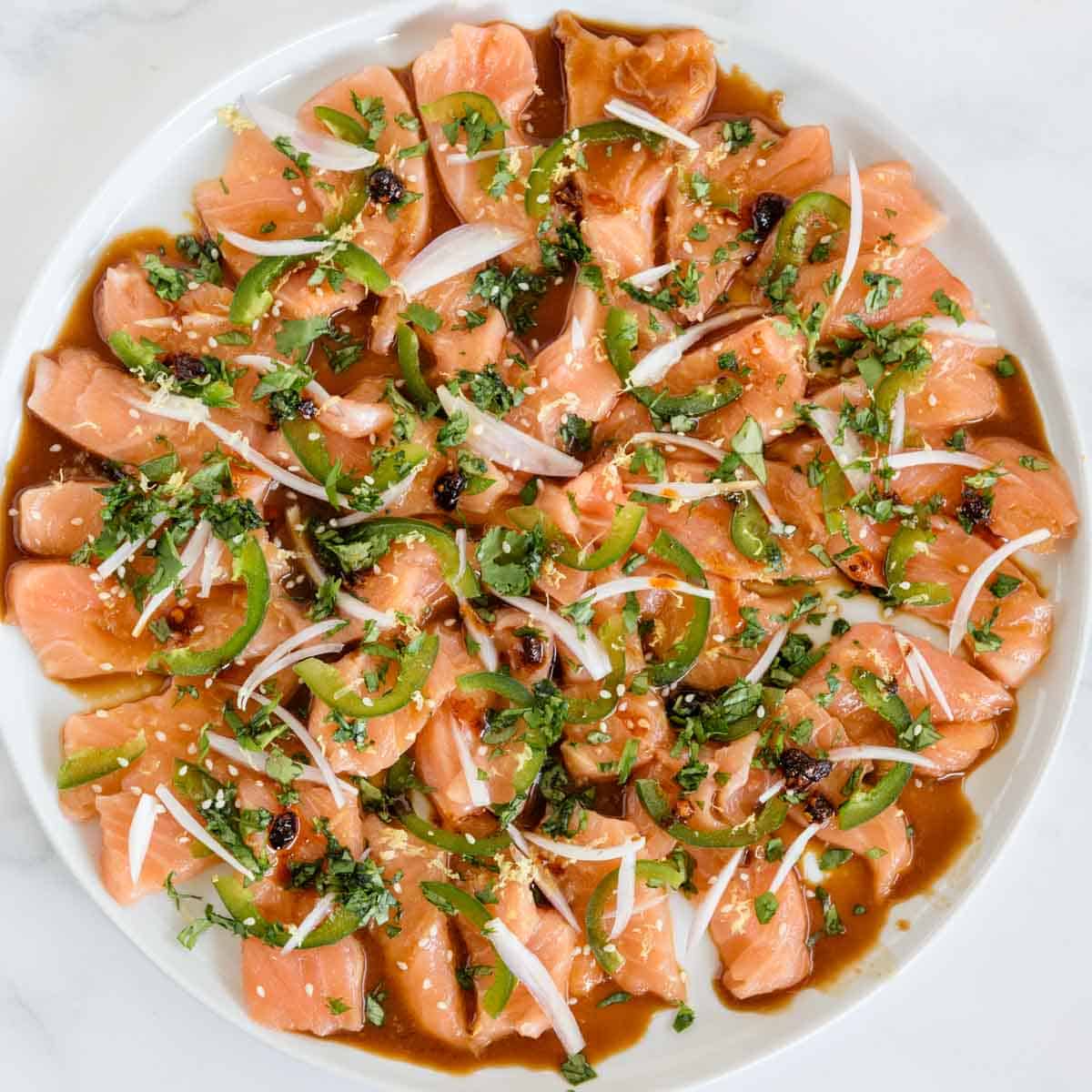 fancy plate of sliced wild salmon topped with shallot, jalapeno, herbs and sauces