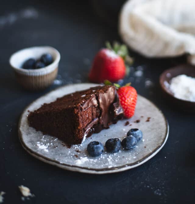 slice of chocolate cake with berries on a plate on dark backdrop
