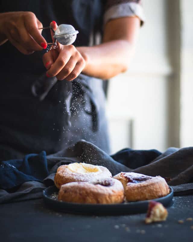 Powdered sugar being sprinkled onto pastries with dark background