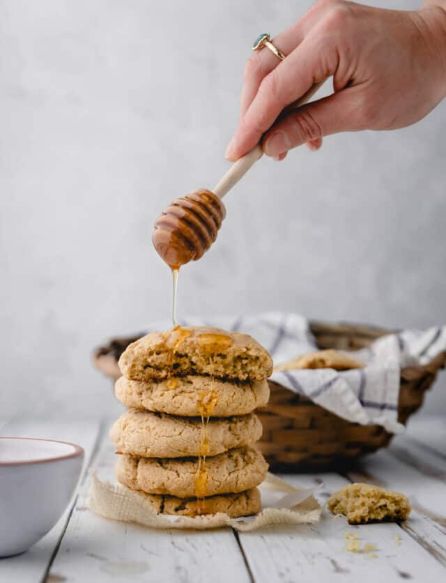 Hand drizzling honey onto a stack of oat flour biscuits