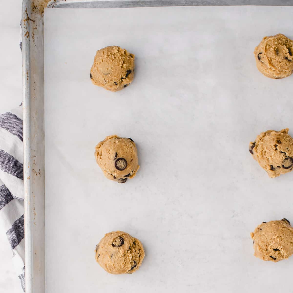 balls of cookie dough laid out on a parchment paper lined baking sheet